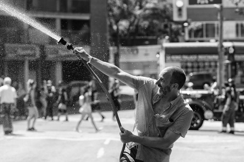 Man with hose spraying water on Church St., Toronto