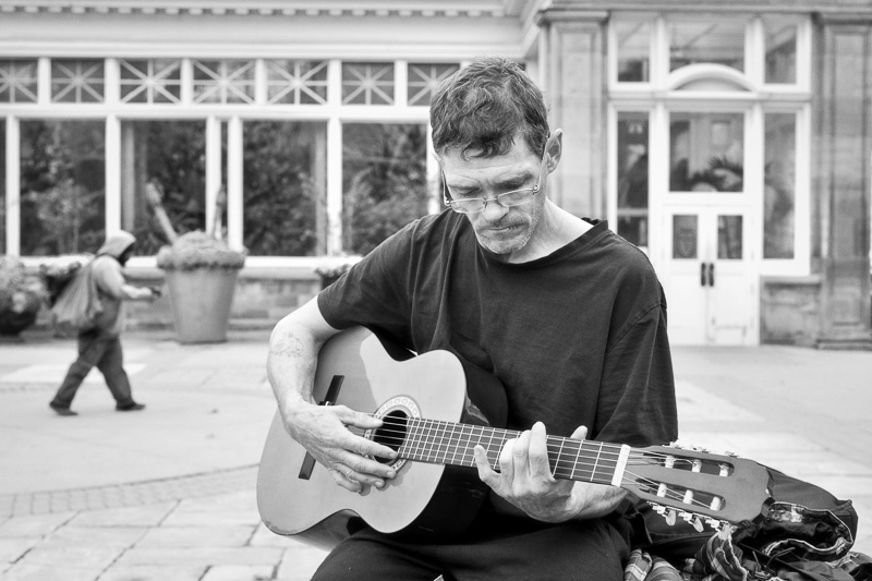 Black and white street portrait of man playing guitar