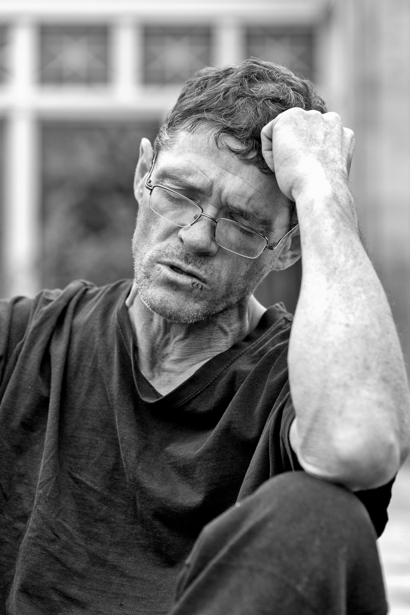 black and white street portrait of man resting elbow on knee