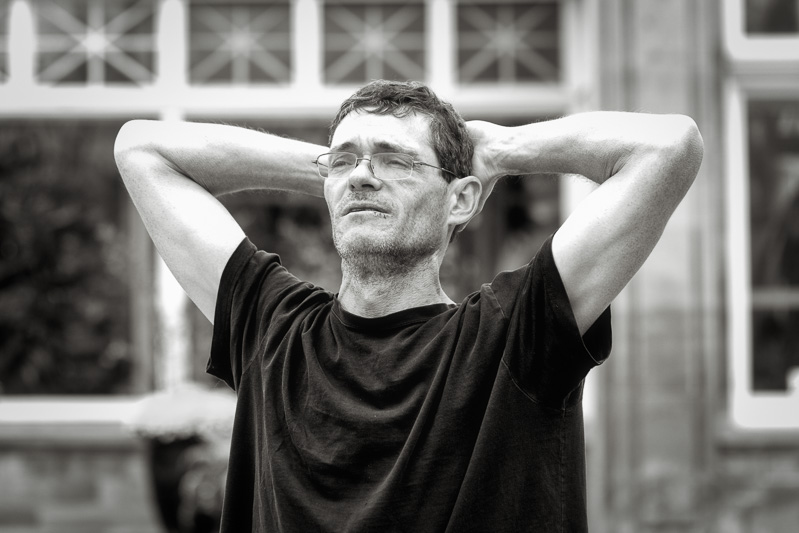 black and white street portrait of man with hands behind head