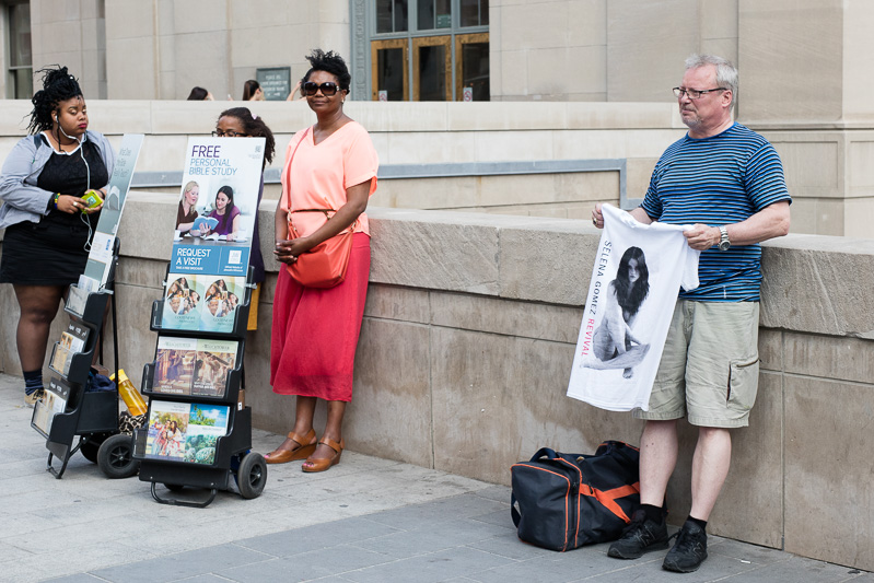 Hawking Selena Gomez T-shirts while a Jehovah's Witness looks on.