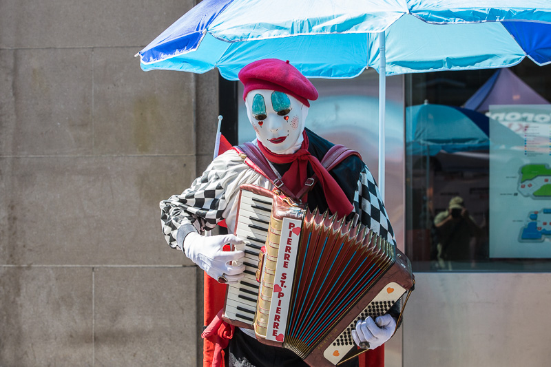 Mime plays an accordion under a blue umbrella