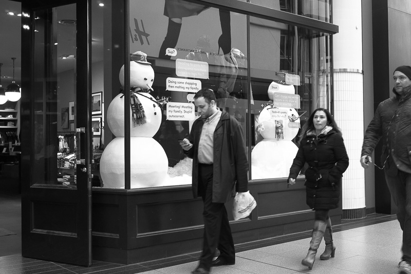 texting in front of shop with snowmen in window
