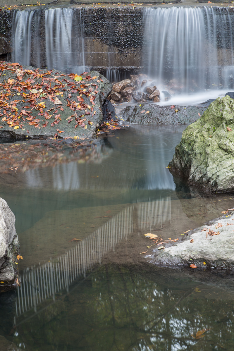 Water pouring from culvert, reflection in pool