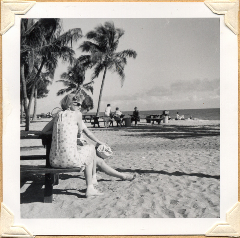 Black and white square photograph of woman on beach with palm trees