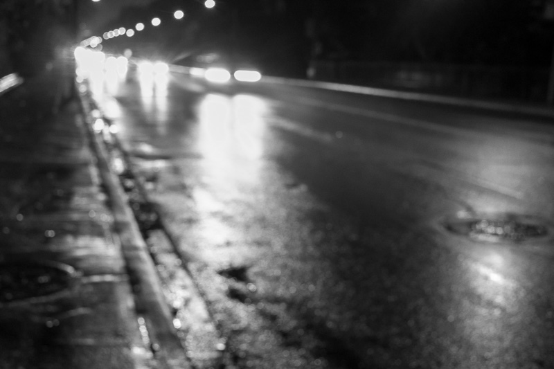 Black and white photograph of car at night passing on wet pavement