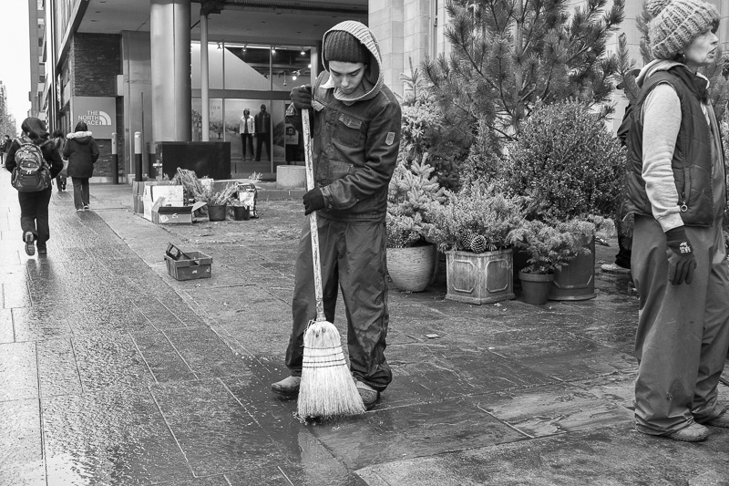 Sweeping sidewalk after setting up greenery on Bloor Street