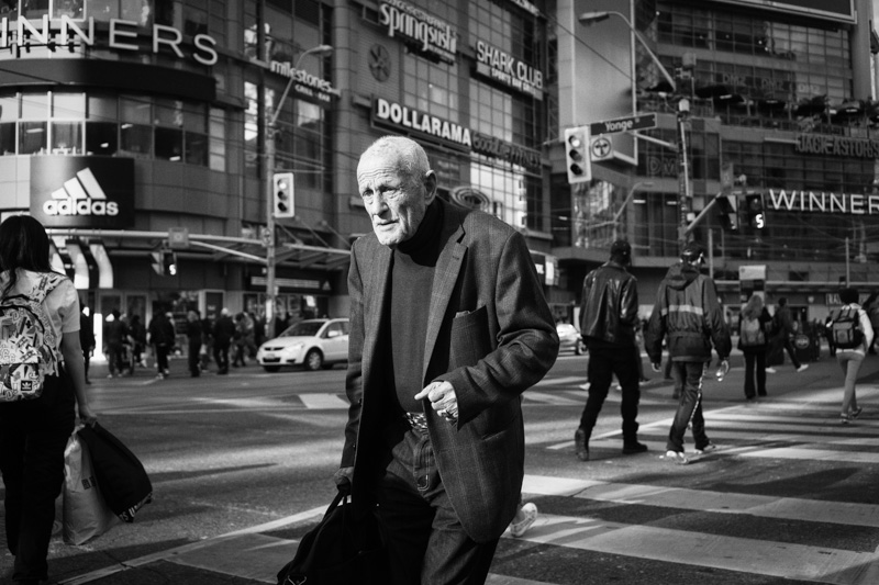 Elderly man crosses the intersection of Yonge and Dundas Streets in downtown Toronto.