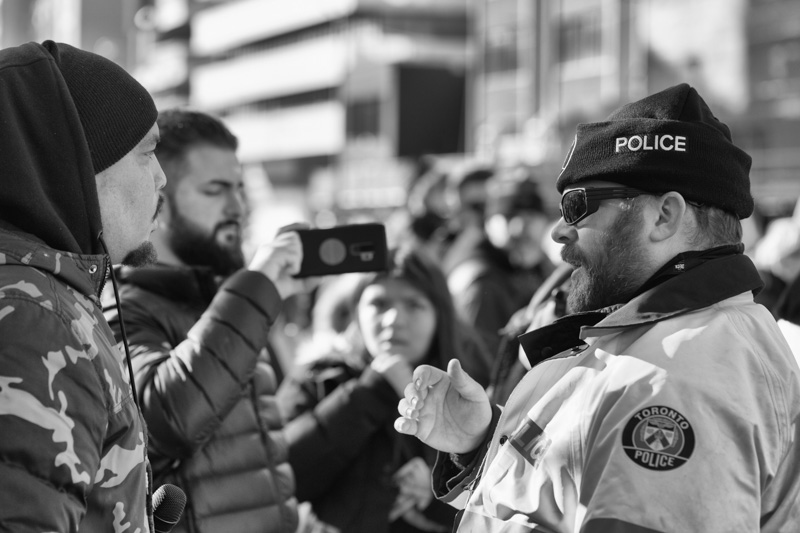 Toronto police officer speaks to man wearing toque and hoodie.