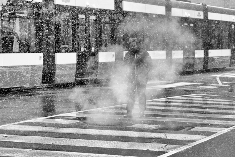 Woman crosses street in snowstorm while enshrouded by steam from a vent.