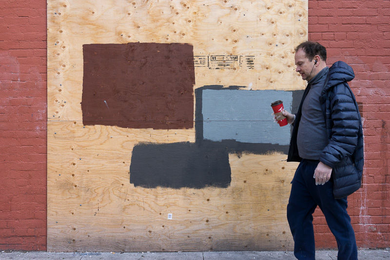 Man holding coffee cup passes in front of a painted plywood panel.