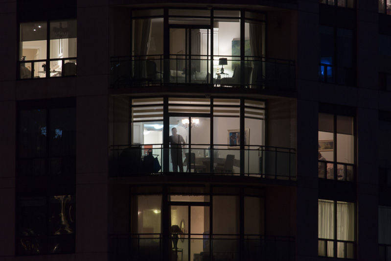 Night shot of man staring out condominium window.