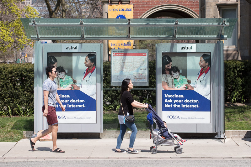 Young family passes bus shelter with advertising promoting vaccinations.