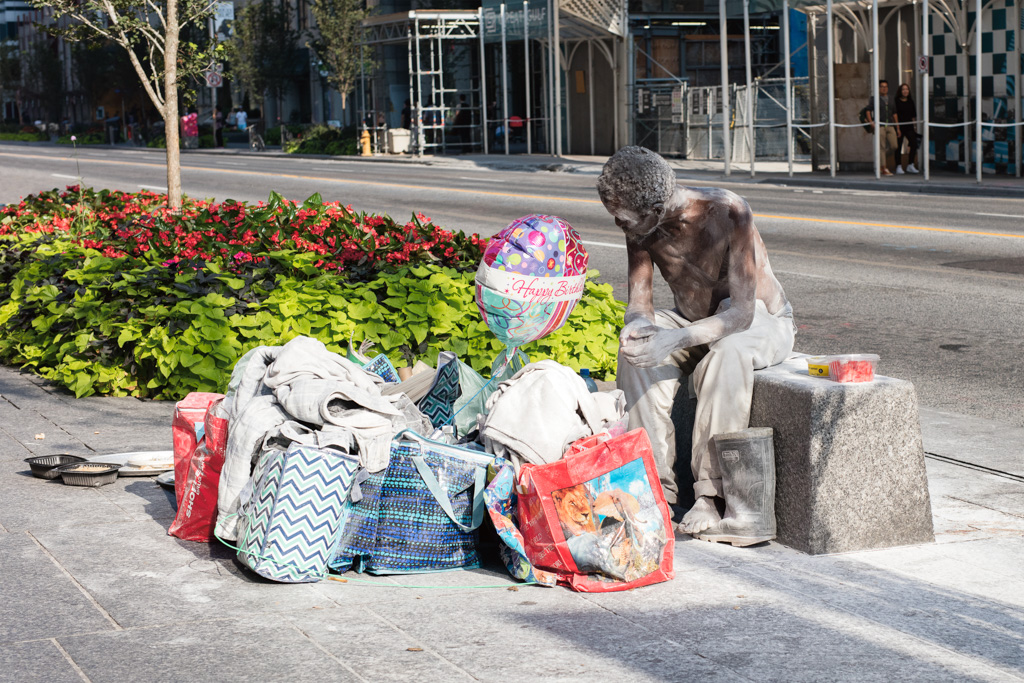 Man sitting with bags and balloon outside the Bloor/Yonge subway station, Toronto.