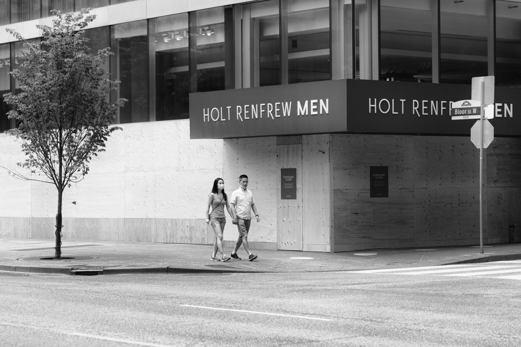 Couple holding hands as they pass a store with windows boarded up.