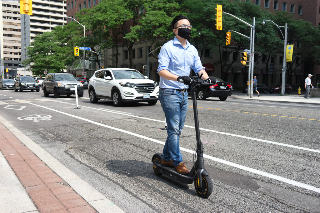 A man wearing a mask rides a scooter along Bloor Street East, Toronto