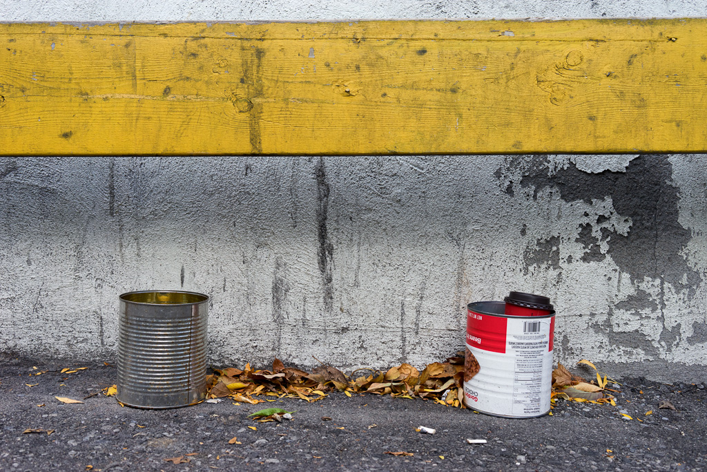 Two empty tin cans sit underneath a yellow board.