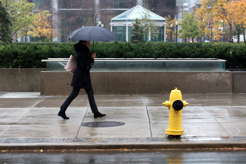 Woman walks past a yellow fire hydrant while holding an umbrella.