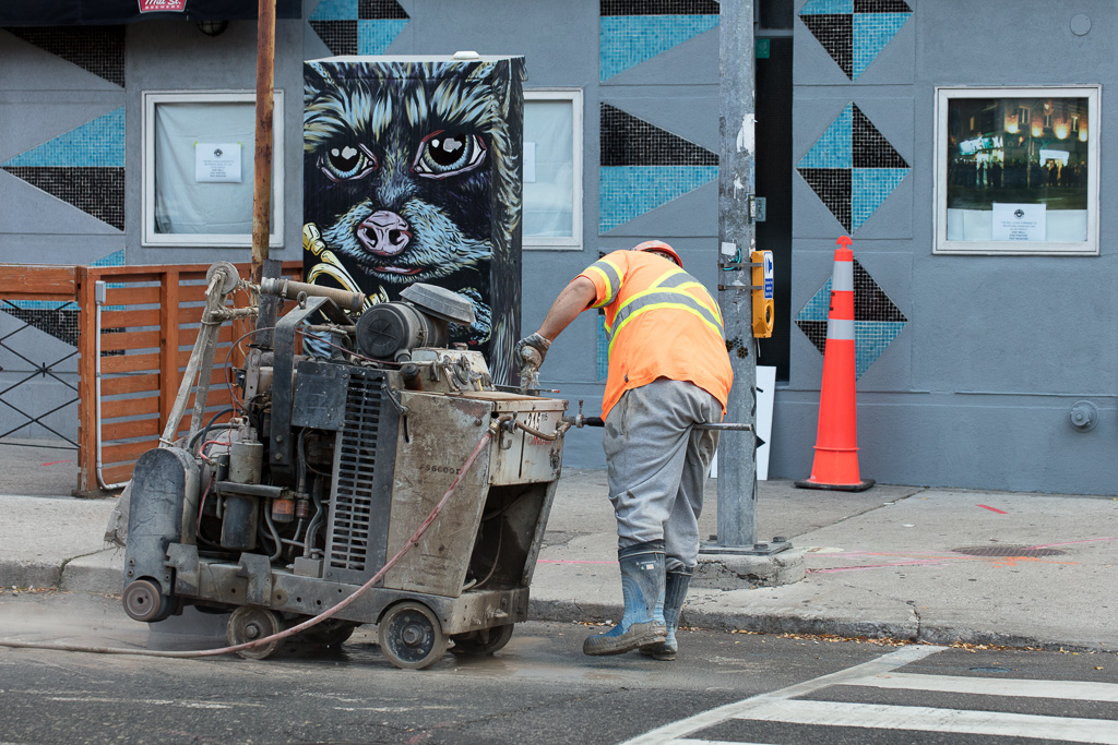 Worker operates saw to cut asphalt.