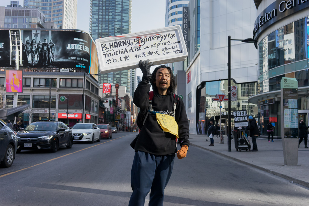 A man stands in the middle of Yonge Street holding a sign over his head.