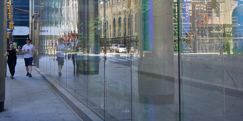 Two people walking between columns and reflective glass windows in downtown Toronto.