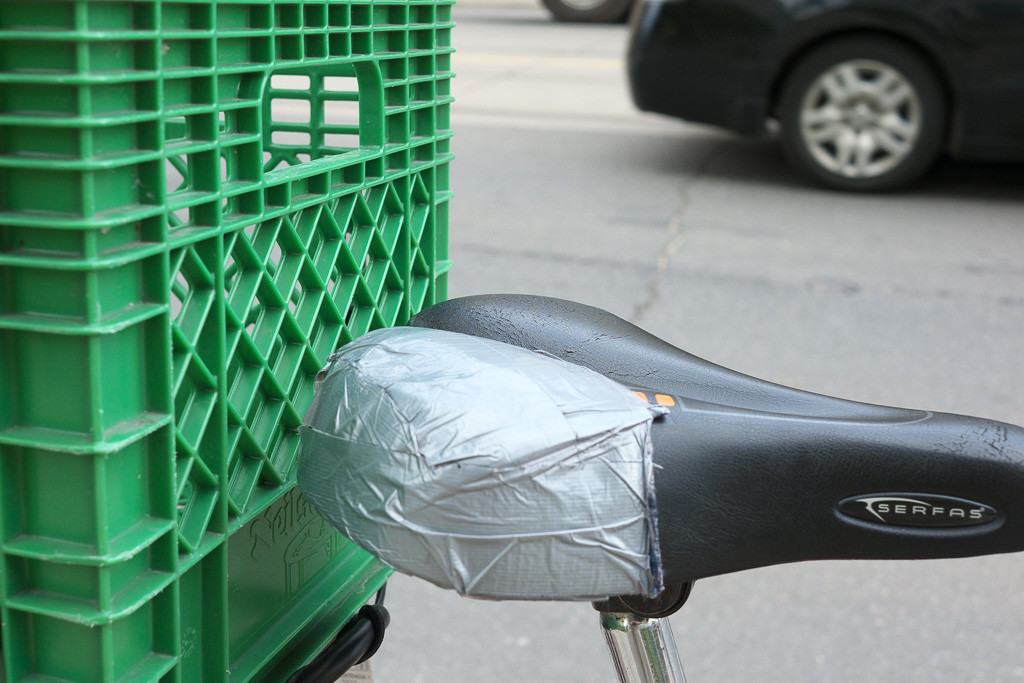 Bicycle seat repaired with duct tape and a green plastic milk crate.