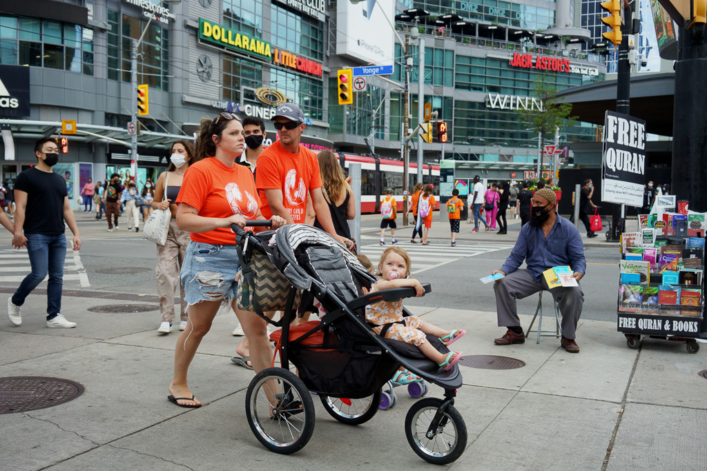 Family dressed in orange "Every Child Matters" T-shirts pushes strollers through Dundas Square, Toronto