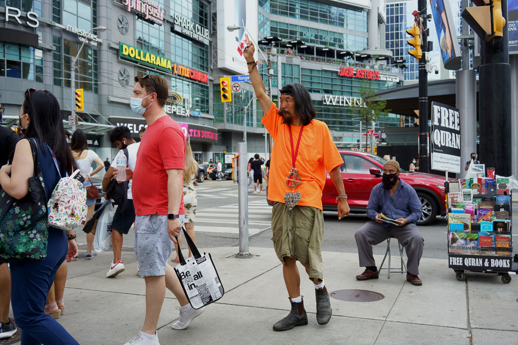 Man in orange T-shirt holds Canadian flag upside down in Dundas Square, Toronto