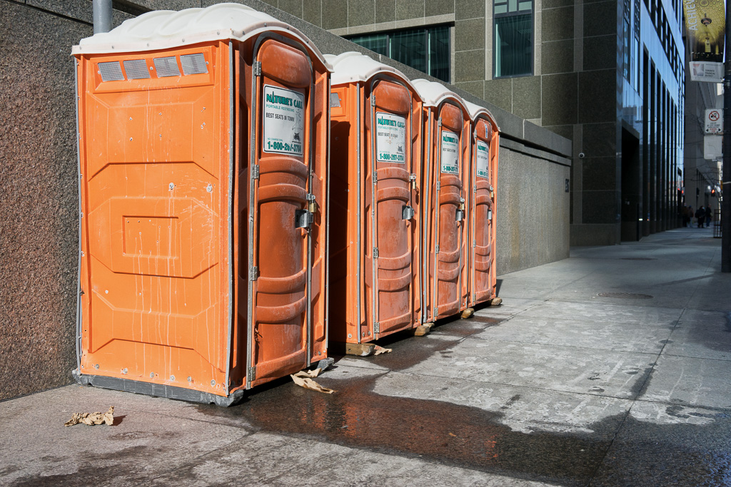 Orange portable toilets in a line on the sidewalk, Wellington Street, Toronto