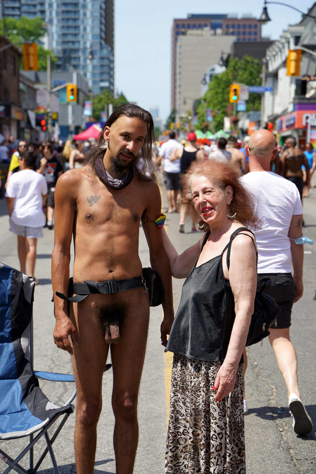 Standing in the middle of Toronto's Church Street, a woman licks her lips while resting a hand on the arm of a man who wears no clothes.