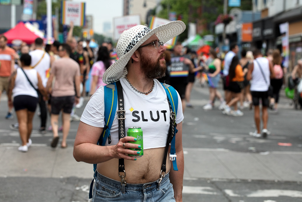 Person walks down the middle of Toronto's Church Street wearing a sun hat and a T-shirt that says "Slut"