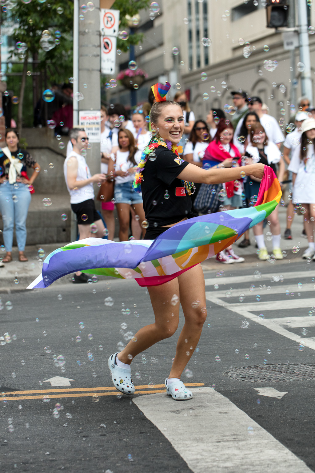 A woman dances through bubbles on Toronto's Church Street while whirling a rainbow flag around her waist.