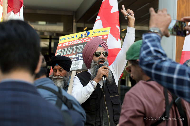 Sikh protester outside the Indian Consulate in Toronto points a finger in the air while speaking into a microphone.